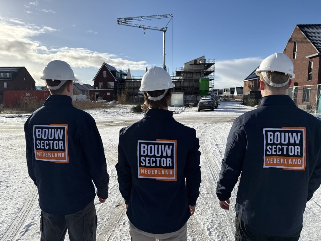 Drie vakmensen van Bouwsector Nederland met witte helm op een besneeuwde bouwplaats met woningen in aanbouw